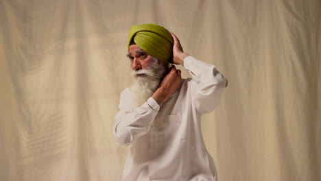 Fotografía-De-Estudio-De-Un-Hombre-Sikh-Mayor-Con-Barba-Atando-Una-Tela-Para-Un-Turbante-Contra-Un-Fondo-Liso-Como-Secuencia,-Parte-3-De-3